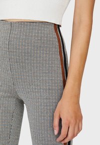 Pantalones de cintura alta con un patrón de pata de gallo, que presentan franjas laterales marrones, un corte ajustado y una tela texturizada.