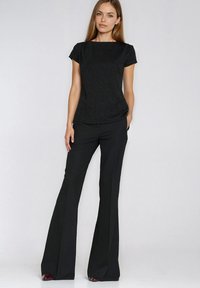 Czarny krótki top z fakturą w połączeniu z wysokim stanem i rozszerzanymi czarnymi spodniami. Charakterystyczne jednolite kolory i czyste linie.