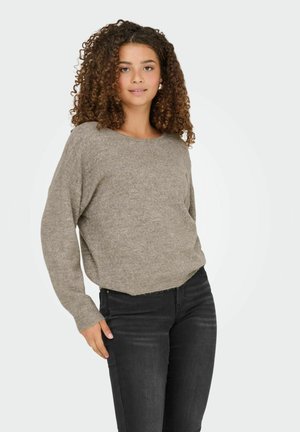 Hellbrauner gestrickter Pullover mit lockerer Passform, rundem Halsausschnitt und langen Ärmeln, kombiniert mit schwarzen eng geschnittenen Jeans. Glatte Textur, lässiges Design.
