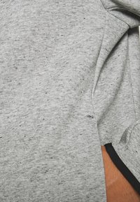 Šedá tkanina s měkkou texturou, zdobená skvrnitými vzory. Obsahuje černý lem poblíž lemu. Na švu jsou viditelné švy.