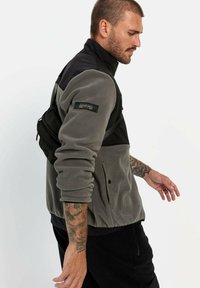Grau Fleecejacke mit schwarzen Akzenten, hohem Kragen, Reißverschluss vorne und einer Tasche. Verfügt über einen strukturierten Stoff und verstellbare Riemen.