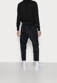 Černé manšestrové jogger kalhoty s elastickým pasem, zúženým střihem nohavic a detaily se zipovými kapsami. Kombinováno s bílými teniskami a ponožkami.