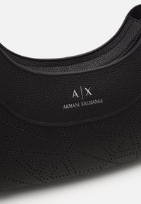 Borsa nera in texture con un motivo geometrico perforato, caratterizzata da un bordo superiore liscio e logo embossato "A|X ARMANI EXCHANGE" in argento.