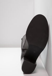 Černá kožená bota s kulatou špičkou, detailem na zip a masivním podpatkem. Podešev je hladká s mírnou texturou, velikost označena jako 37.