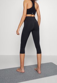 Leggings de sport noirs coupe crop en tissu stretch, avec une taille haute et une coupe longueur cheville. Portés avec un soutien-gorge de sport noir assorti.