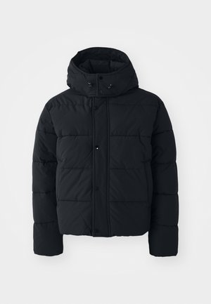 La veste rembourrée noire présente un col haut, des boutons-pression et une texture matelassée. Elle est dotée d'une capuche pour plus de chaleur et a une coupe ample.