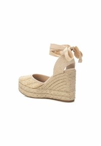 Cuña de esparto beige con parte superior tejida, tira texturizada y lazo. Presenta una cuña envuelta en yute y un diseño de punta redondeada.