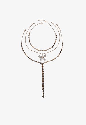 Tre collane in tono oro, una con un ciondolo floreale trasparente, una con maglie a forma di diamante e una con un lungo nappina di diamanti collegati.