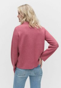 Rosa pulloversweater tillverkad av mjukt material. Har en avslappnad passform, neddragna axlar och vida ärmar. Bärs med ljusblå jeans.