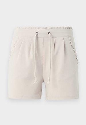 Light beige shorts with an elastic waistband, drawstring, side pockets, and ruffle detailing along the pocket edges. Soft fabric texture.