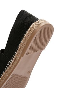 Zwarte canvas espadrille met jute touwaccenten op de zool, voorzien van een getextureerde rubberen basis en gestikte details langs de rand.