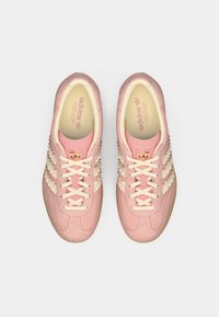 Roze sportieve schoenen met textuurpanelen, crèmekleurige strepen en crèmekleurige veters. Ronde neus met een rubberen zool en een zachte stofvoering aan de binnenkant.