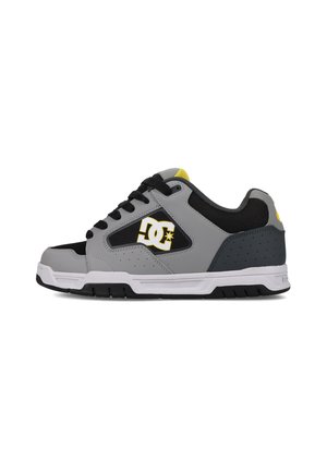 Baskets basses grises et noires avec des accents jaunes, en cuir et en mesh, avec des détails perforés et une semelle en caoutchouc blanc. Logo DC sur le côté.