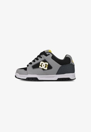 Szare i czarne niskie sneakersy z żółtymi akcentami, wykonane z materiałów skórzanych i siatkowych, z perforowanymi detalami oraz białą gumową podeszwą. Logo DC z boku.