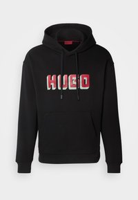 Felpa nera con cappuccio e tasca a marsupio frontale, caratterizzata da un ampio logo "HUGO" in lettere bloccate rosse e bianche. Tessuto morbido con cappuccio regolabile tramite stringhe.