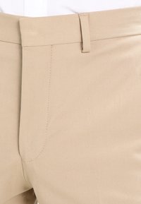 Beiga byxor med en slät textur, som har en rak front, en enda bältesöga och subtila stygn för ett strömlinjeformat utseende.