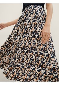 Jupe midi fleurie en marine avec des fleurs orange et blanches. Tissu fluide avec des plis, dotée d'une taille ajustée et d'une coupe décontractée.