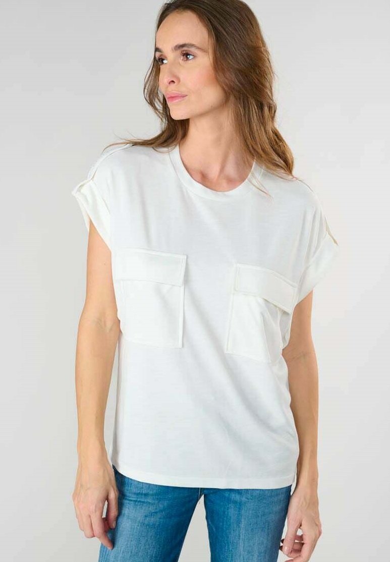 Top bianco a maniche corte con due tasche frontali, vestibilità morbida, collo rotondo e texture liscia, abbinato a jeans blu.