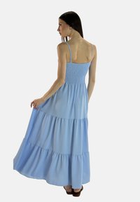 Helles blaues Maxikleid mit dünnen Trägern, gerafftem Oberteil und gestuftem Rock. Hergestellt aus fließendem Stoff mit weicher Textur, verfügt es über ein geschichtetes Design.