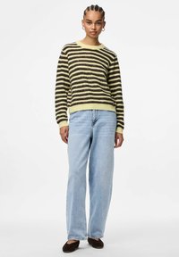 Striped sweater in yellow and dark brown, featuring a crew neck and ribbed cuffs, paired with light blue wide-leg jeans and dark flats.