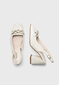 Białe lakierowane buty slingback na kwadratowym nosku i szerokim obcasie. Posiadają dekoracyjny akcent w postaci łańcuszka na wierzchu.