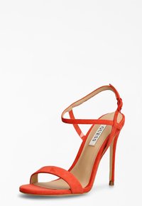 Røde ruskinds højhælede sandaler med åben tå og ankelrem, der har en slank stilettohæl og en glat sål. Accenterne er minimale.