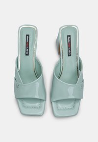 Mintvihreät patenttinaarmilla varustetut slingback-kengät, joissa on neliönmuotoinen kärki, leveä vyö edessä ja vaatimaton lohkare korko. Musta logotieto sisällä.