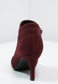 Bordowe zamszowe botki na wysokim obcasie sięgające kostki, z ostrym noskiem, zakrzywionym kształtem i zamkiem błyskawicznym z boku. Teksturowana cholewka z gładką podeszwą.
