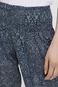 Nærbillede af en hånd, der hviler ved siden af løstsiddende marineblå bukser med hvide indviklede blomster- og prikmønstre og elastisk taljebånd.