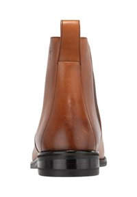 Slät brun läderankelboot med svart sula och klack, sedd bakifrån med en dragflik och subtila söm detaljer.