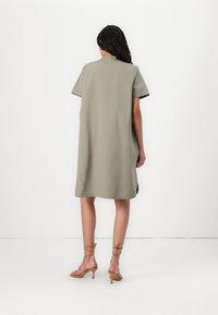 Kratka rokava, obleka do kolen v svetlo olivno zeleni tkanini, z udobnim krojem, stranskimi razpoki in okroglo vratno odprtino. V kombinaciji z golimi sandalčki na peto.