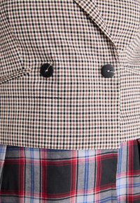 Tissu vichy marron et noir avec deux boutons noirs ; superposé à un motif écossais multicolore en gris, rouge et bleu.