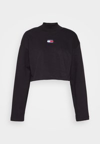 Black cropped long-sleeve top with a high collar and a small rectangular logo patch in red, white, and blue on the chest. Soft fabric.
