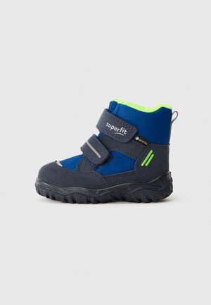 Bottes d'enfants bleu marine avec un tissu texturé et une semelle en caoutchouc. Les caractéristiques incluent deux bandes Velcro et des accents vert fluo.