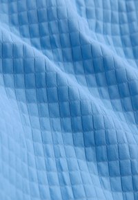Tissu bleu clair avec un motif carré matelassé, montrant des plis doux et des variations de texture sous un éclairage diffus.
