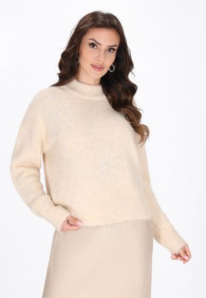 Beige, fluffy trui met een opstaande kraag en lange mouwen. Voorzien van bloemenpatronen van strass op de voorkant en geribbelde manchetten.
