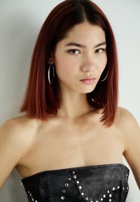 Top senza spalline nero con finitura testurizzata, decorato con borchie argentee, indossato da una persona con capelli castani lisci e orecchini a cerchio.