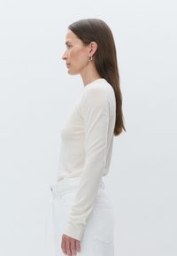 Un pull à manches longues beige clair en matière douce, assorti à un pantalon taille haute blanc. Il présente des poignets côtelés et un design ajusté.
