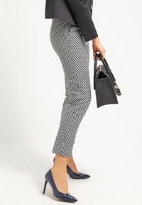 Zwart-witte, gestreepte broek met een slim fit ontwerp, gecombineerd met marineblauwe Hakken en een gestructureerde zwarte handtas.