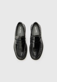 Mocassins en cuir noir avec une finition lisse, des accents cloutés sur le dessus et une semelle épaisse pour un confort accru.
