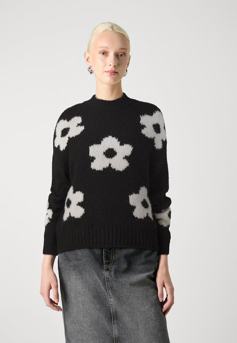 Maglione nero lavorato a maglia con grandi motivi floreali bianchi, scollatura rotonda e polsini e orlo a coste. Tessuto morbido e testurizzato.