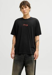 Zwarte katoenen t-shirt met een rode "Lucky You" grafiek op de borst. Losse pasvorm met korte mouwen, gecombineerd met donkere jeans.