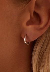 Silberner Creolenohrring mit polierter Oberfläche, der ein sauberes, rundes Design und eine mittlere Dicke aufweist, getragen an einem durchgestochenen Ohr.