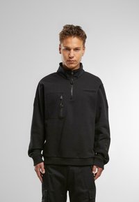 Črn fleece pulover z visokim ovratnikom, polovičnim zadrgo spredaj in dvema žepoma na zadrgo. Teksturna tkanina z gladko površino, manšete z zadrgami.