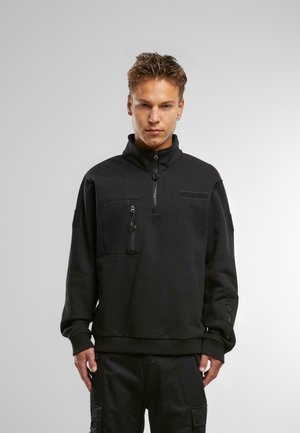 Čierny fleece pulóver s vysokým golierom, predným polovičným zipsom a dvoma zipsovými vreckami. Textúrovaná tkanina s hladkým povrchom, manžety so zipsami.