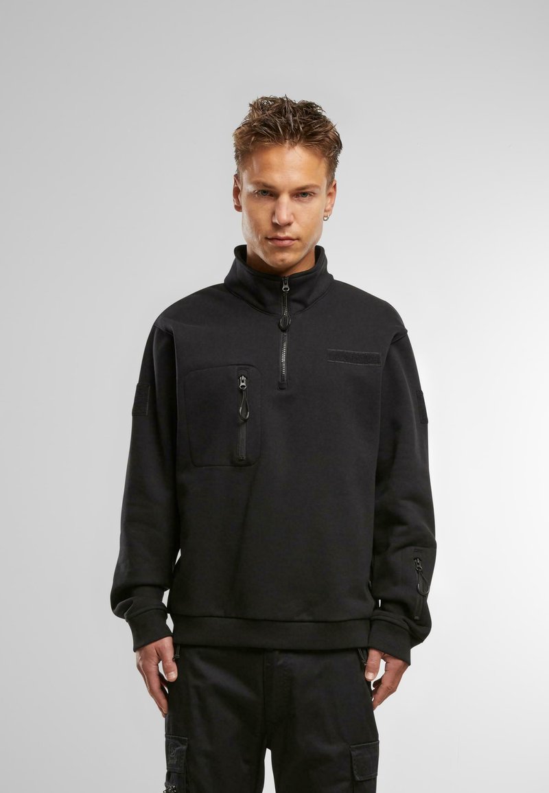 Črn fleece pulover z visokim ovratnikom, polovičnim zadrgo spredaj in dvema žepoma na zadrgo. Teksturna tkanina z gladko površino, manšete z zadrgami.