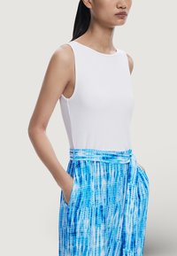 T-shirt sans manches blanc à côtes associé à un pantalon en tie-dye bleu avec des poches latérales et une taille nouée.