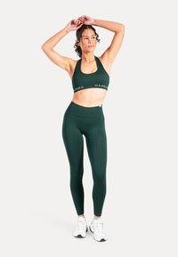 Mörkgrön sport-bh och matchande högmidjade leggings av stretchigt tyg. Har ett logoband på bh:n, slät textur och figursydd design.