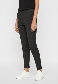 Pantaloni su misura grigio scuro con una vestibilità slim, caratterizzati da una texture liscia, tasche laterali e risvolti. Abbinati a sneaker bianche.
