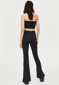 Czarny, dopasowany, krótki top o prostym kroju z elastycznego materiału, zestawiony z czarnymi spodniami rozszerzającymi się na dole. Oba elementy cechują się gładką teksturą.
